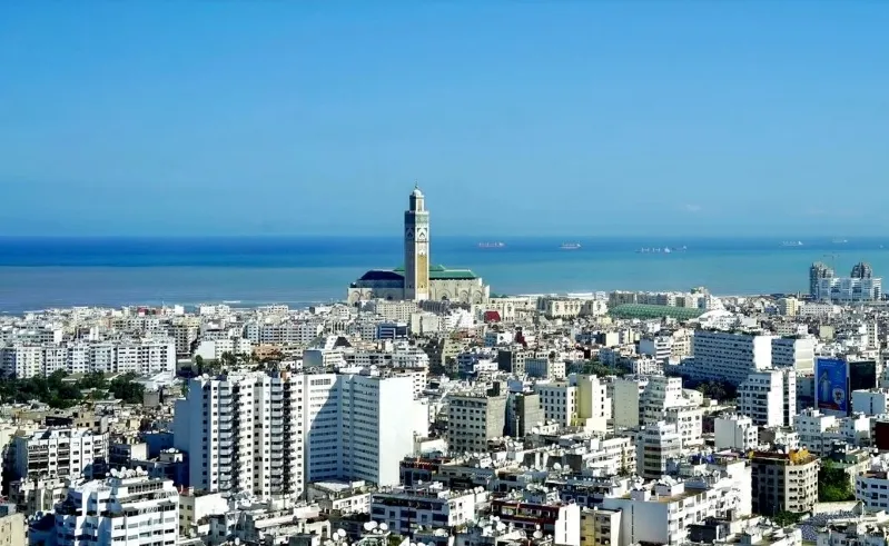 A skyline of Casablanca, Morocco, featuring tall buildings and a prominent clock tower against a clear blue sky.