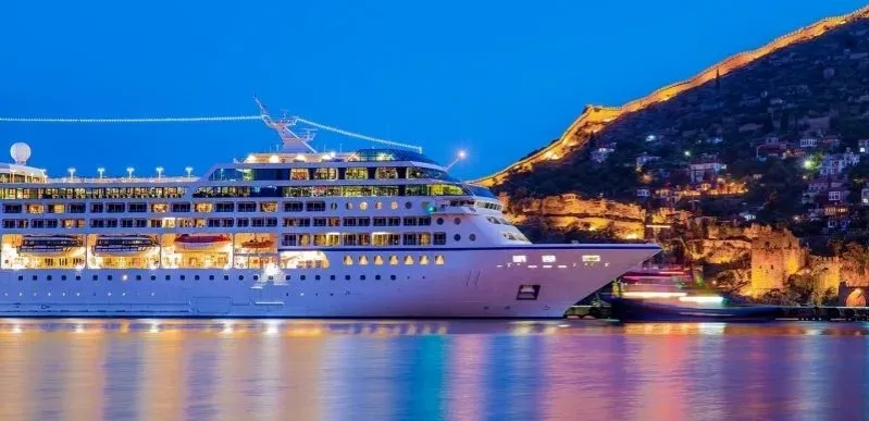 A cruise ship illuminated at night, docked in a harbor with city lights reflecting on the water in Casablanca.
