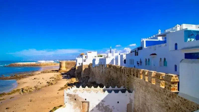 White buildings line the beach beside the ocean, showcasing luxury accommodations on a Morocco tour.