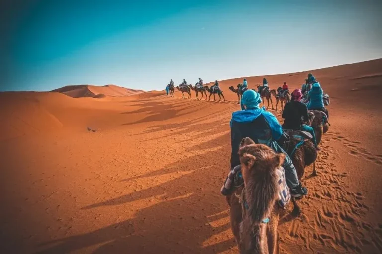 A group of people riding camels across a vast desert landscape under a clear blue sky.