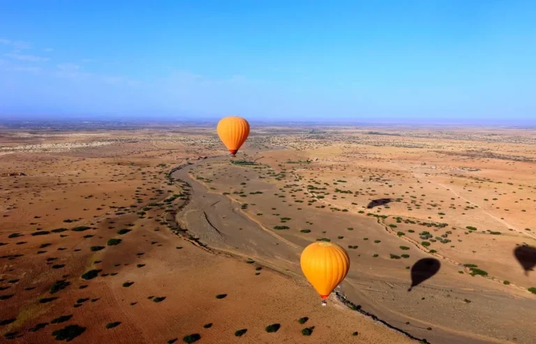 Hot air balloons soaring over a vast desert landscape near Marrakech, showcasing vibrant colors against the sandy terrain.