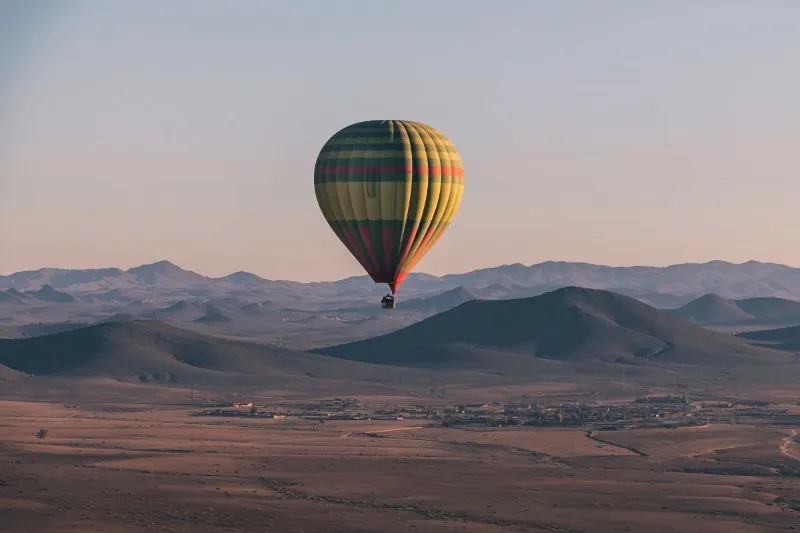A colorful hot air balloon soaring over the vast desert landscape near Marrakech by air balloon, showcasing the arid terrain below.