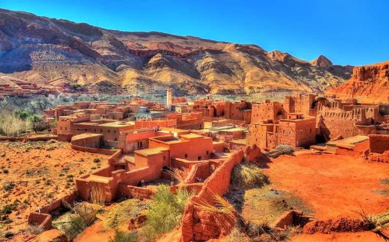 A panoramic view of the village of Atlas nestled in the desert, showcasing its traditional architecture against a sandy backdrop.