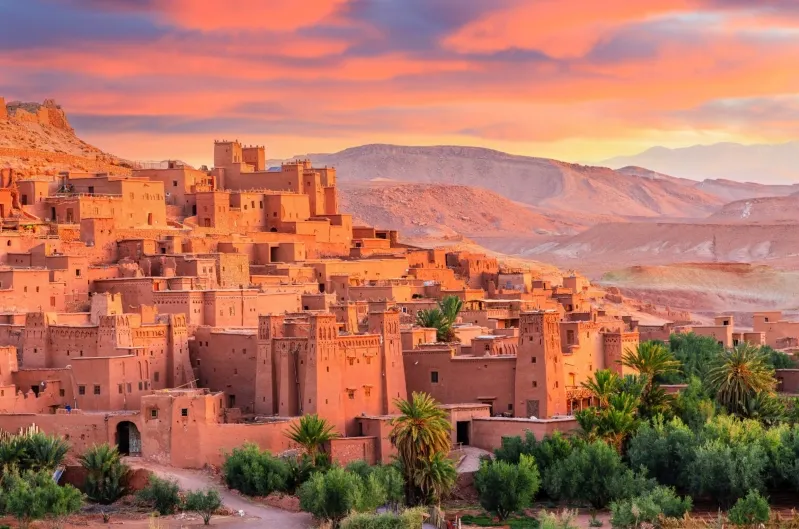 Sunset over a Moroccan city, showcasing vibrant colors and silhouettes, promoting tour packages to Morocco.