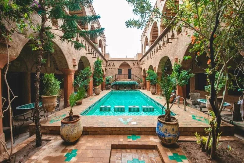 A serene courtyard of an old building featuring a tranquil pool, set against the backdrop of a Moroccan desert tour.