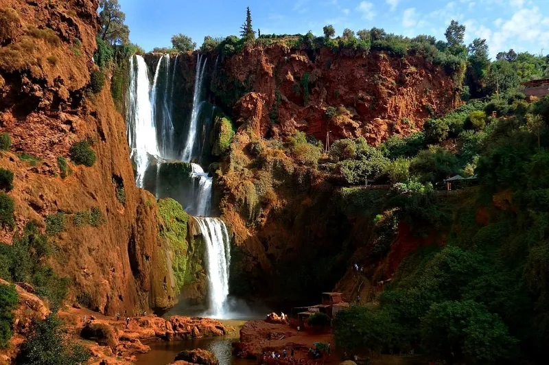 A waterfall cascades down surrounded by striking red rocks in the scenic Ourika Valley.