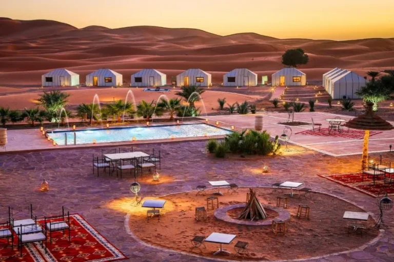 Sunset over the pool and patio area at Merzouga desert camp, highlighting the serene desert landscape.