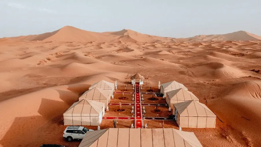 A desert camp in Morocco featuring tents and a car, set against the vast sandy landscape.