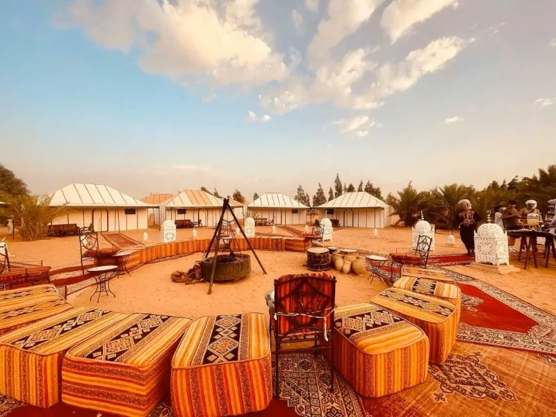 A view of Merzouga desert camp featuring multiple tents and chairs set up in the sandy landscape.
