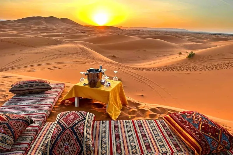A table and chairs set against a desert backdrop, illuminated by a vibrant sunset in Morocco.