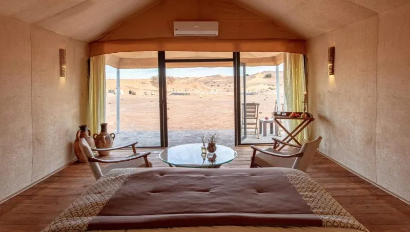 A cozy bedroom overlooking the vast Merzouga desert, featuring warm tones and natural light.
