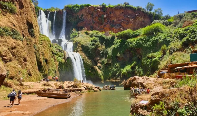 A group of people stands near the Ouzoud Cascades, enjoying the view of the majestic waterfall.