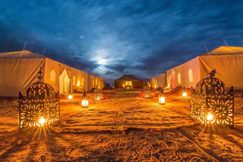 The moon illuminates tents in the desert during a trip to Marrakech, creating a serene nighttime atmosphere.