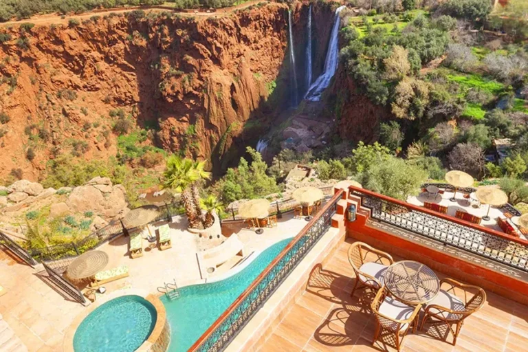 A serene pool and patio with a view of Ouzoud Cascades, featuring a waterfall and majestic mountains in the background.
