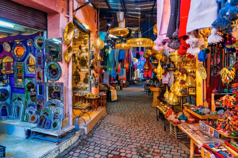 A narrow alley in Souk Marrakech lined with vibrant, colorful items on display for shoppers and visitors.