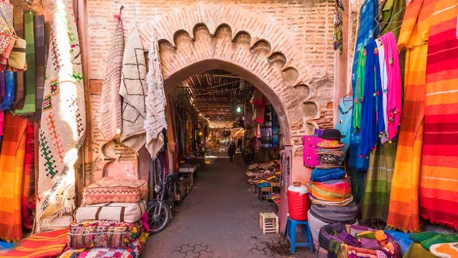 The lively Souk in Marrakech, Morocco, featuring colorful market stalls and shoppers exploring traditional goods and crafts.