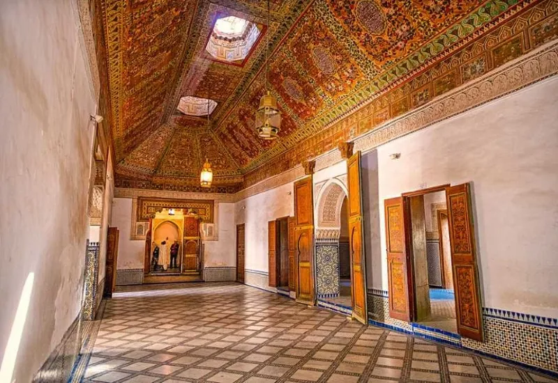 Ornate hall with intricate geometric ceiling, colorful tile work, and arched doorways, exuding an elegant and historic ambiance.Between Marrakech Morocco attractions.