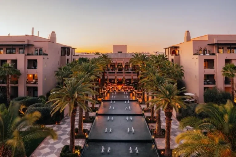 Sunset view of a Marrakech resort featuring palm trees and a serene pool, creating a tranquil atmosphere.