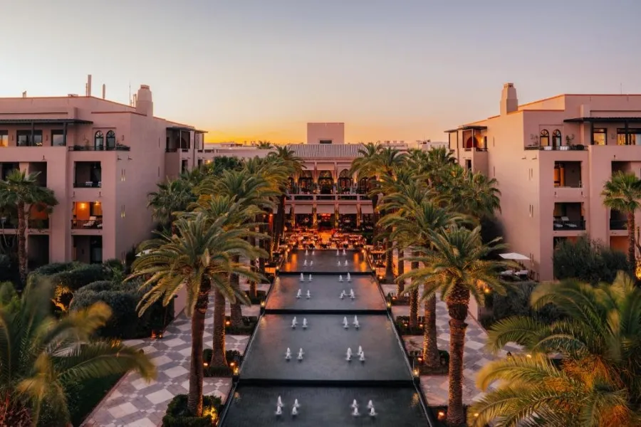 Sunset view of a Marrakech resort featuring palm trees and a serene pool, creating a tranquil atmosphere.